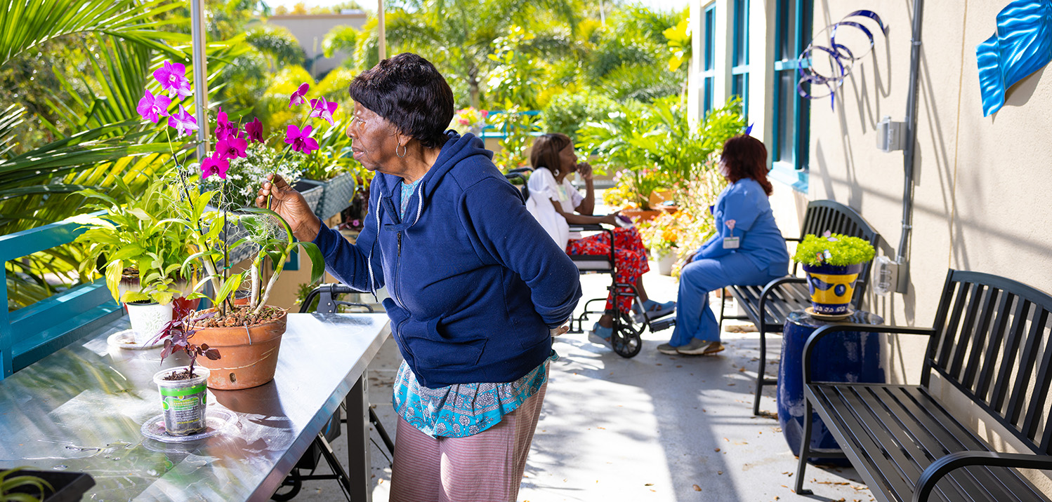 Participant smelling flower in garden with aide and another participant in the background