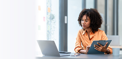 female looking at laptop holding clipboard